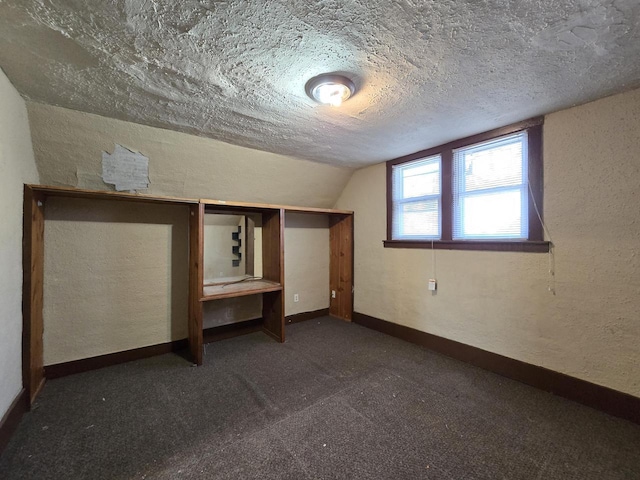 bonus room featuring a textured ceiling, lofted ceiling, and dark colored carpet