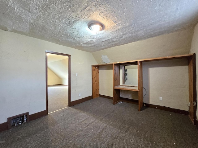 unfurnished bedroom with lofted ceiling, dark carpet, and a textured ceiling