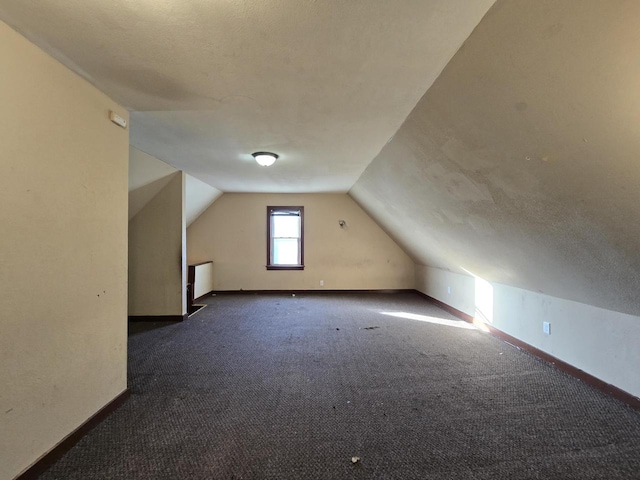 bonus room with a textured ceiling, vaulted ceiling, and dark carpet