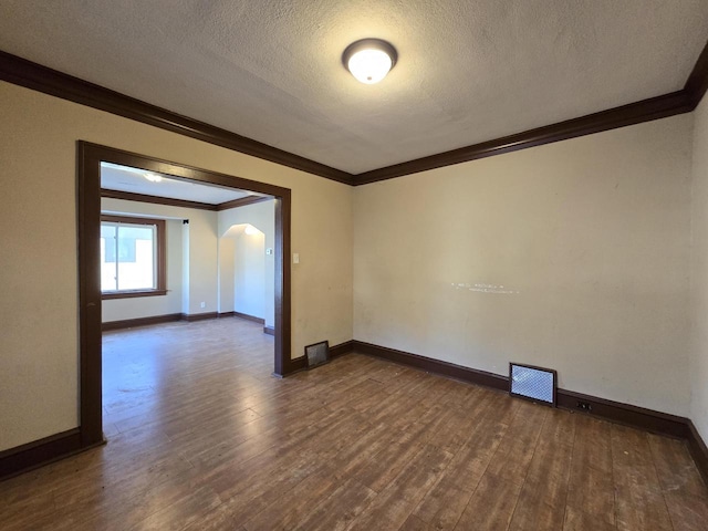 empty room featuring a textured ceiling, dark wood-type flooring, and ornamental molding