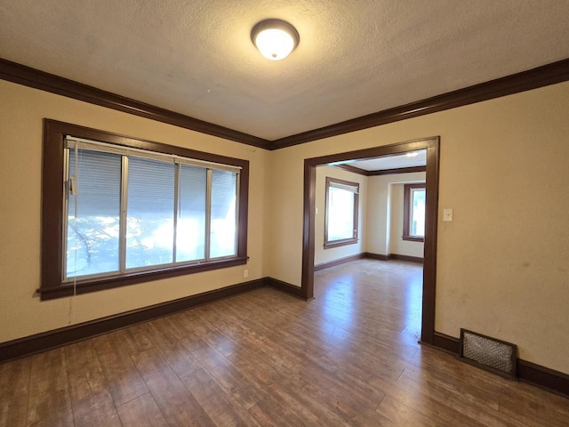 empty room with a textured ceiling, ornamental molding, and dark hardwood / wood-style floors