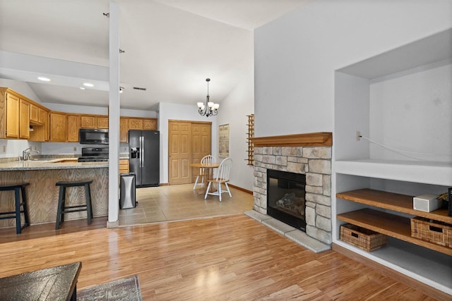 living room featuring sink, a chandelier, light hardwood / wood-style flooring, and a stone fireplace