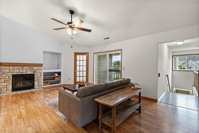 living room featuring hardwood / wood-style floors, a stone fireplace, vaulted ceiling, ceiling fan, and built in shelves