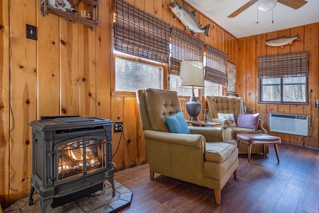 sitting room with dark wood-type flooring, wooden walls, a wealth of natural light, and a wood stove