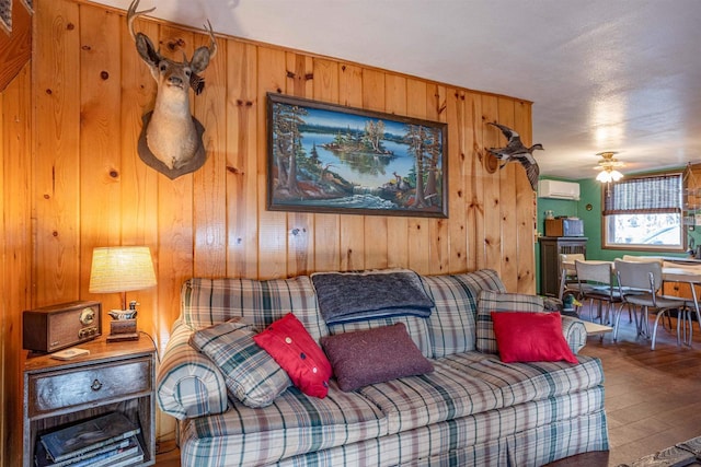 living room featuring hardwood / wood-style floors, wood walls, ceiling fan, and a wall mounted AC