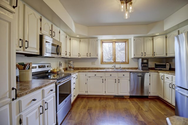 kitchen featuring appliances with stainless steel finishes, dark wood-type flooring, white cabinets, and sink