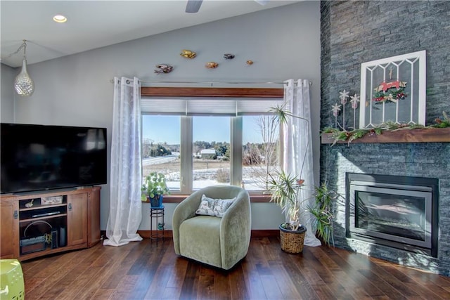 sitting room with ceiling fan, vaulted ceiling, dark hardwood / wood-style flooring, and a stone fireplace