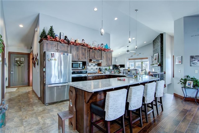 kitchen featuring stainless steel appliances, ceiling fan, kitchen peninsula, backsplash, and a breakfast bar