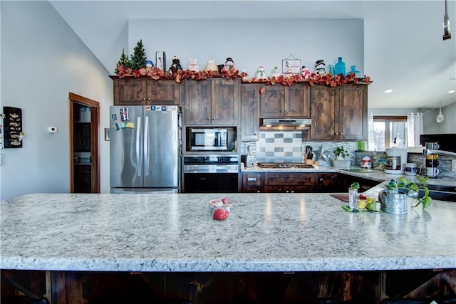 kitchen featuring vaulted ceiling, stainless steel appliances, a breakfast bar, decorative backsplash, and dark brown cabinets