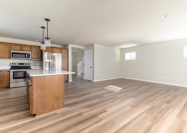 kitchen featuring pendant lighting, a kitchen island, light hardwood / wood-style flooring, and appliances with stainless steel finishes