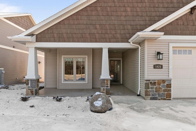 snow covered property entrance featuring a garage and covered porch