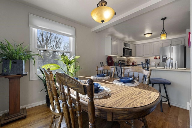 dining space featuring sink, wood-type flooring, and beamed ceiling