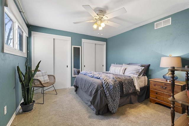 bedroom with ceiling fan, light carpet, and multiple closets