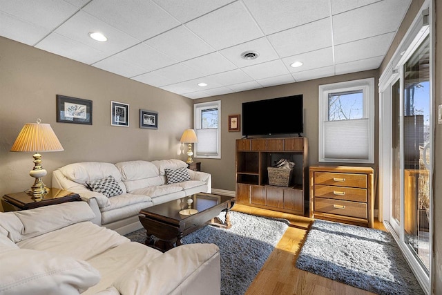 living room featuring a healthy amount of sunlight, wood-type flooring, and a paneled ceiling