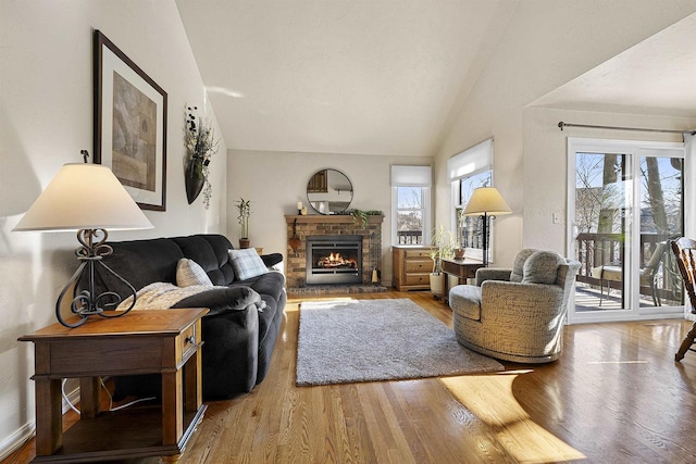 living room with wood-type flooring, lofted ceiling, and a stone fireplace