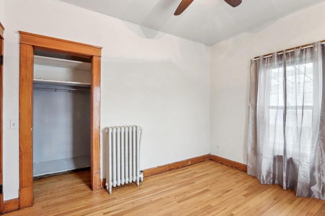 unfurnished bedroom featuring ceiling fan, radiator, a closet, and light hardwood / wood-style flooring