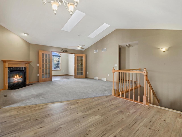 unfurnished living room featuring french doors, a fireplace, light hardwood / wood-style floors, ceiling fan, and lofted ceiling with skylight