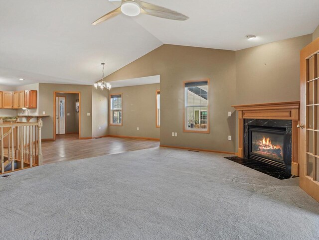 unfurnished living room with light colored carpet, lofted ceiling, a fireplace, and ceiling fan with notable chandelier