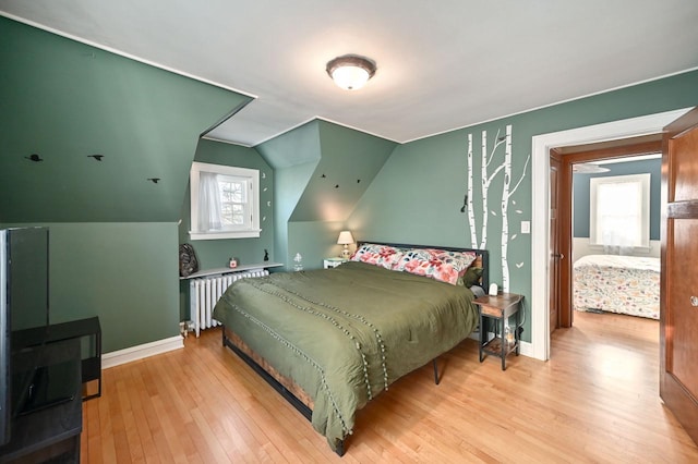 bedroom featuring vaulted ceiling, light hardwood / wood-style floors, radiator heating unit, and multiple windows