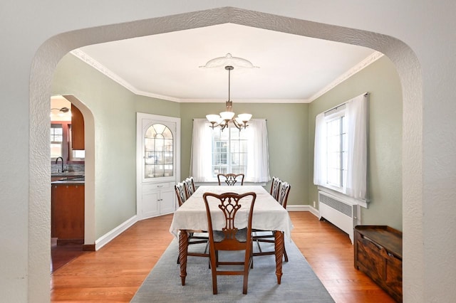 dining space featuring sink, light wood-type flooring, radiator heating unit, a chandelier, and crown molding