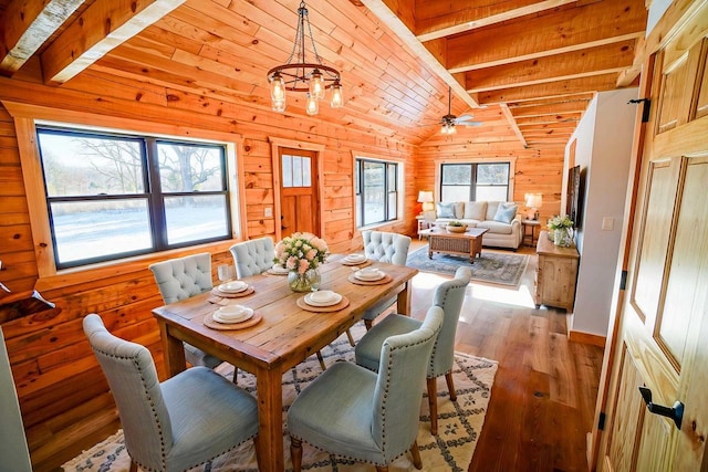 dining space with wooden walls, wooden ceiling, light hardwood / wood-style flooring, ceiling fan with notable chandelier, and lofted ceiling with beams