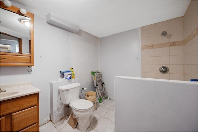 bathroom with toilet, vanity, tile patterned flooring, and tiled shower