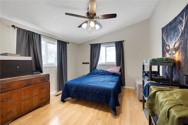 bedroom featuring ceiling fan, light wood-type flooring, vaulted ceiling, and a textured ceiling