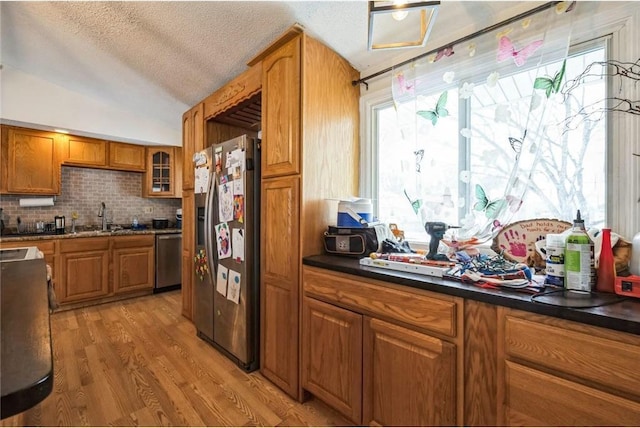 kitchen featuring a textured ceiling, lofted ceiling, light hardwood / wood-style flooring, decorative backsplash, and appliances with stainless steel finishes