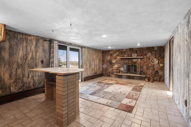 unfurnished living room with a stone fireplace, a baseboard radiator, and wood walls