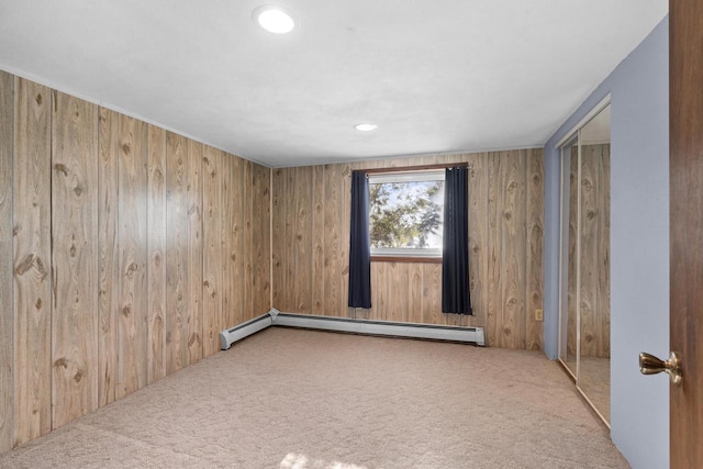 carpeted spare room featuring baseboard heating and wooden walls