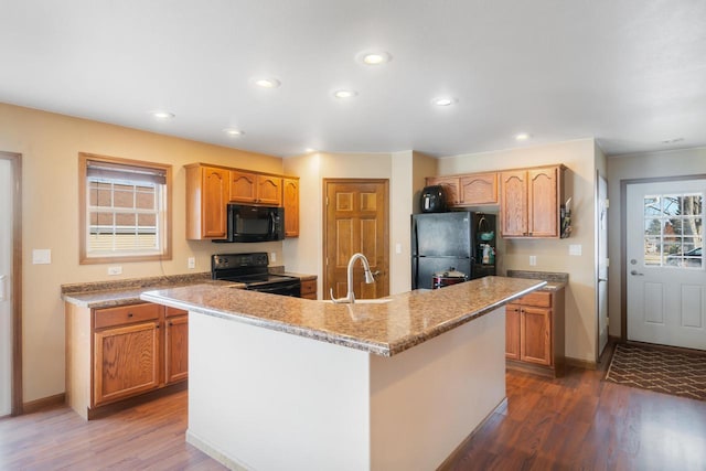 kitchen with black appliances, an island with sink, light stone countertops, dark hardwood / wood-style flooring, and sink