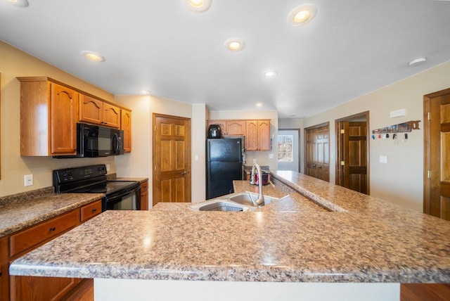 kitchen with black appliances, sink, light stone counters, and a center island with sink