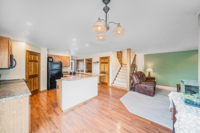 kitchen featuring light hardwood / wood-style flooring, black appliances, hanging light fixtures, a kitchen island with sink, and a notable chandelier