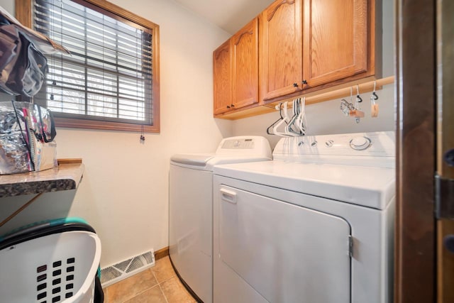 laundry area featuring washing machine and clothes dryer, light tile patterned floors, and cabinets