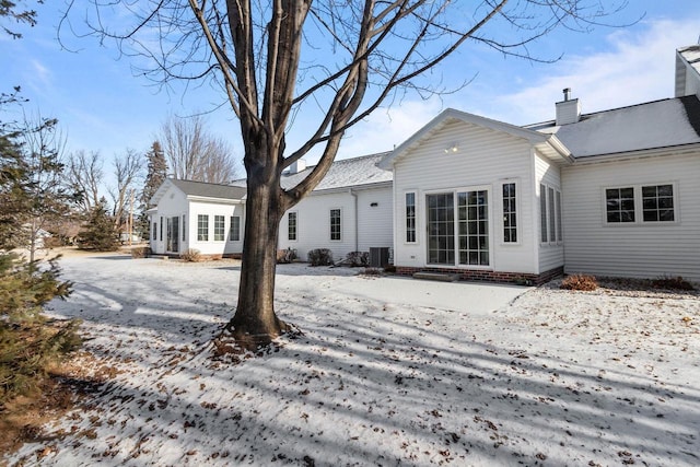 snow covered rear of property featuring central AC