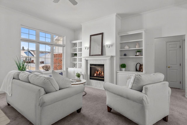 living room with ceiling fan, ornamental molding, a high end fireplace, built in shelves, and light colored carpet