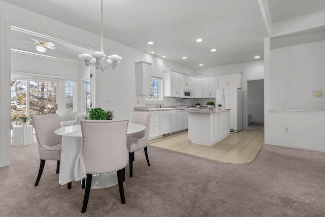 carpeted dining area with ornamental molding, sink, and ceiling fan with notable chandelier