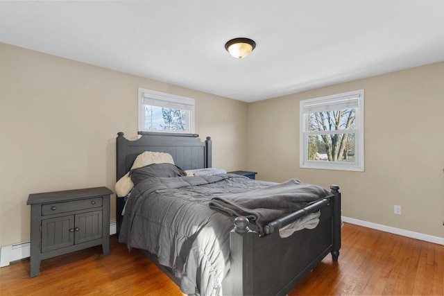 bedroom with wood-type flooring, multiple windows, and a baseboard heating unit