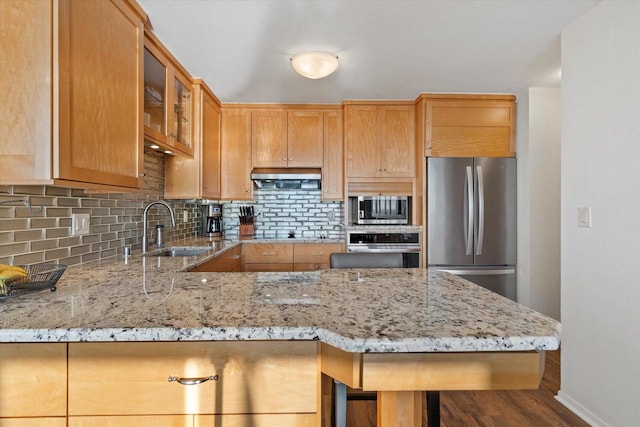 kitchen with appliances with stainless steel finishes, a breakfast bar, light stone counters, sink, and tasteful backsplash