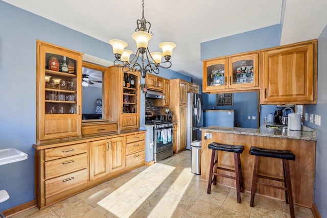 kitchen with light stone counters, kitchen peninsula, ceiling fan with notable chandelier, gas stove, and a breakfast bar