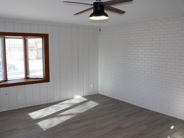 empty room featuring brick wall, dark hardwood / wood-style flooring, and ceiling fan