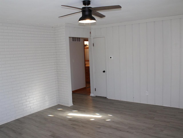 spare room featuring ceiling fan, dark hardwood / wood-style flooring, and brick wall