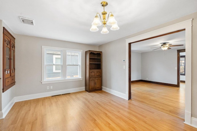 empty room with ceiling fan with notable chandelier and light hardwood / wood-style floors