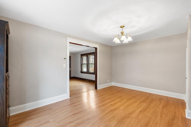 spare room with a chandelier and light wood-type flooring