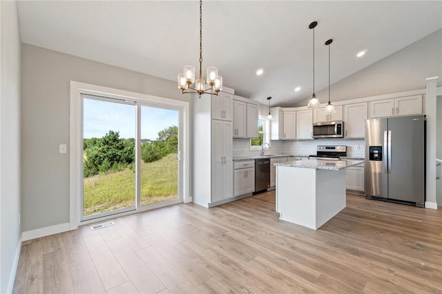 kitchen with stainless steel appliances, decorative light fixtures, light stone counters, lofted ceiling, and a kitchen island