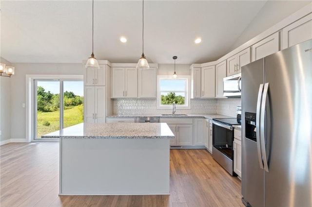 kitchen with stainless steel appliances, a center island, light stone counters, white cabinets, and decorative light fixtures