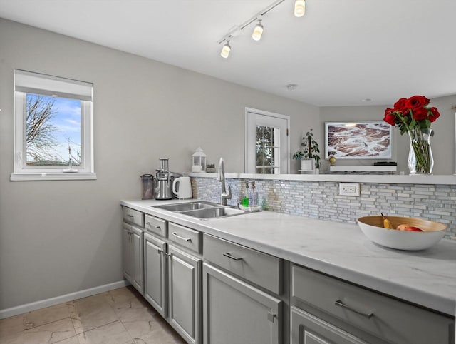 kitchen with decorative backsplash, light stone countertops, gray cabinetry, and sink