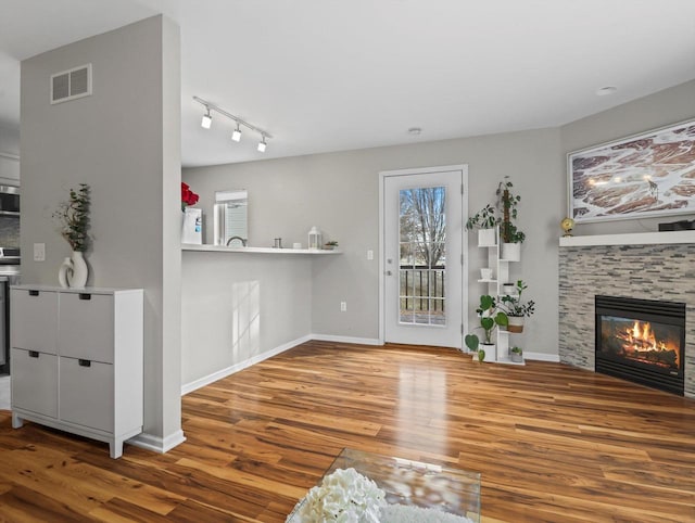 unfurnished living room with hardwood / wood-style floors, rail lighting, and a stone fireplace