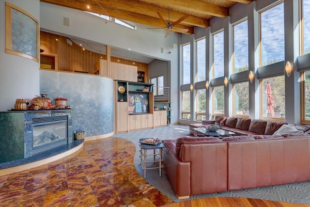 living room with a high ceiling, beam ceiling, ceiling fan, and wooden ceiling