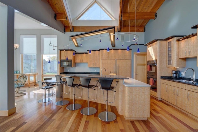 kitchen featuring sink, a center island with sink, black appliances, beam ceiling, and light brown cabinets